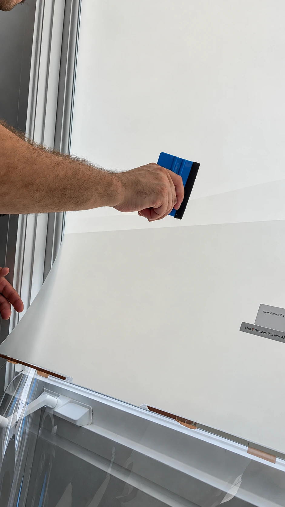 An installer pressing PDLC film onto a window with a blue squeegee